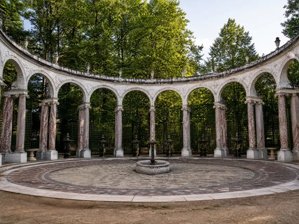 Ein kreisförmiges Boskett aus Marmorbögen mit Brunnen in der Mitte, umgeben von hohen Bäumen